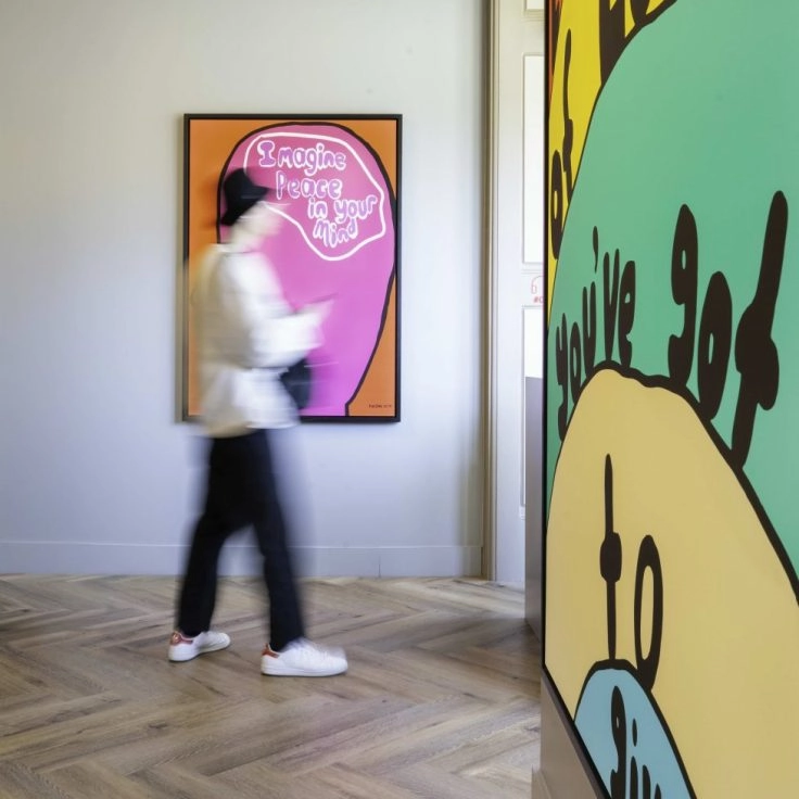 Visitor walking past colorful text-based artwork by Robbie Williams at Moco Museum Amsterdam.
